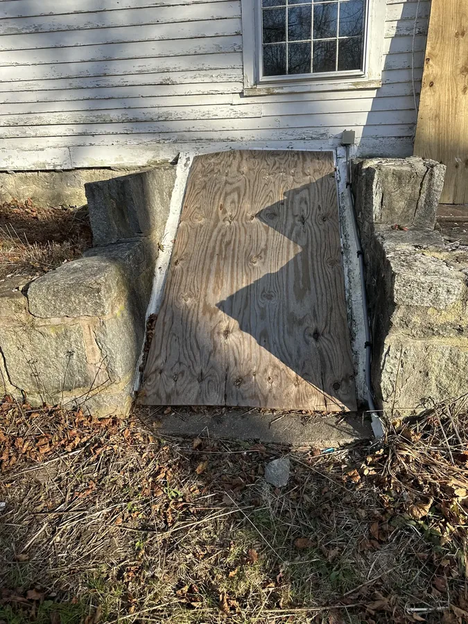 A cellar bulkhead entrance, boarded over, set between two stone foundation piers