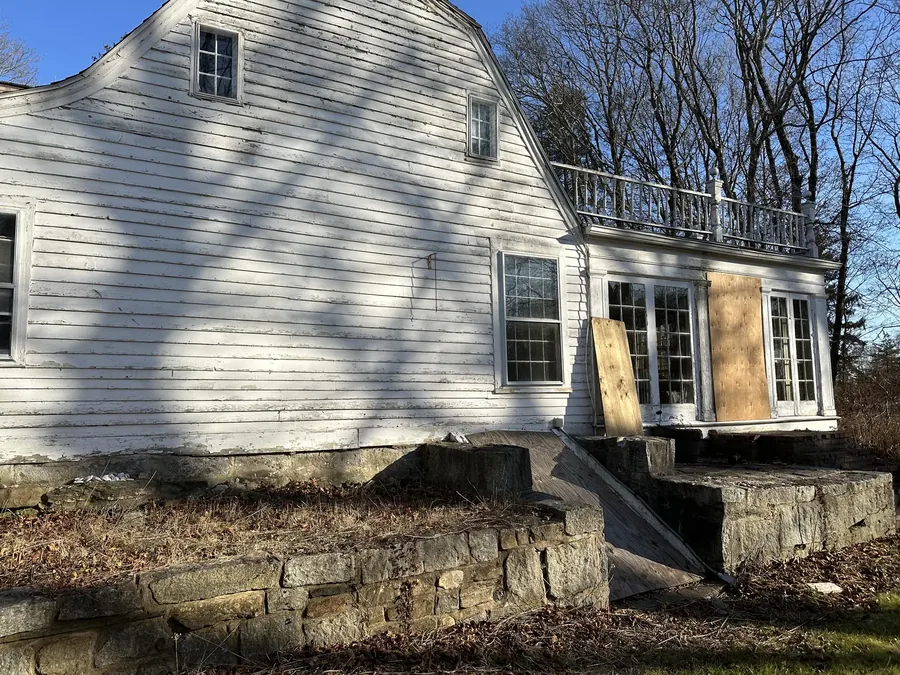 A side entrance to the sunroom, boarded over, with the roofline balustrade visible above