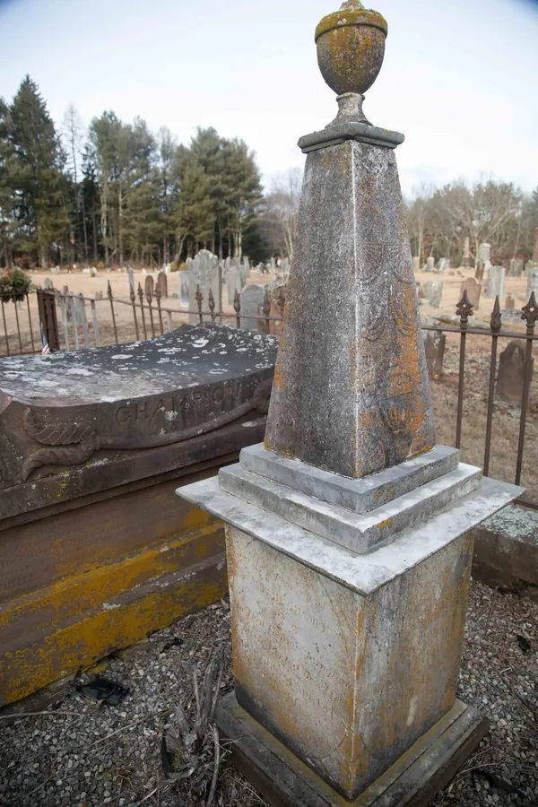 A weathered stone obelisk with an urn finial standing beside the Champion family tomb in Westchester Cemetery