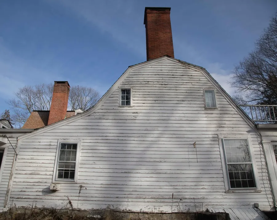 A low winter view of the gambrel roof and its two brick chimneys against a blue sky