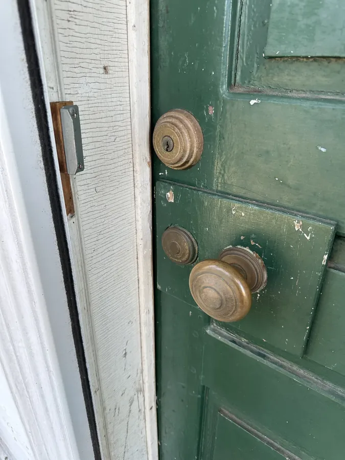 A weathered green door with a set of vintage brass doorknobs and a deadbolt