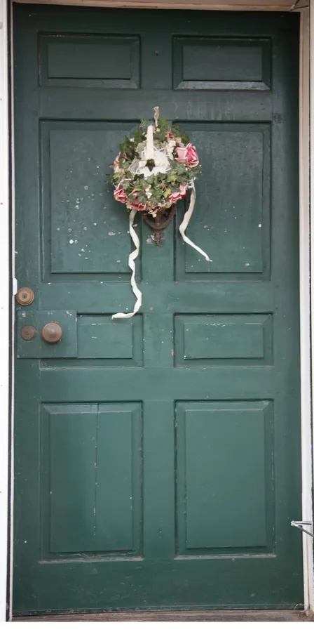 The house's weathered green entry door, with an antique floral wreath hanging on the knocker