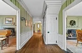 A central hallway with wide-plank wood floors, striped and floral wallpaper, and rooms opening on either side