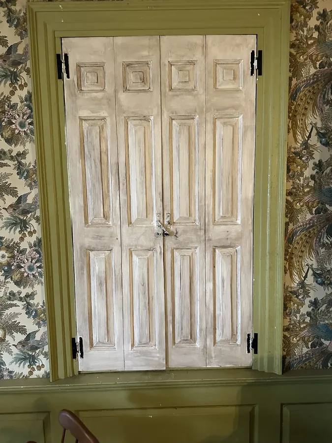 Folding interior shutters in a room papered with a bold floral print