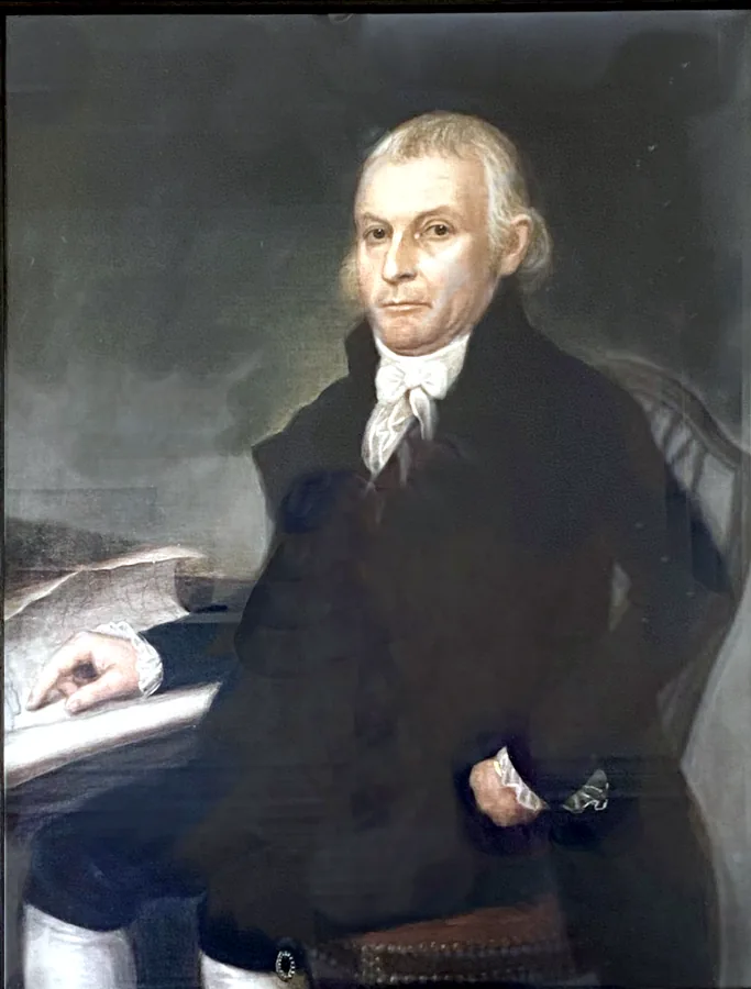 Portrait of General Henry Champion, seated in a dark coat with a white cravat, pointing to a paper on a table