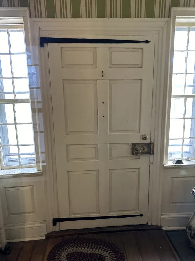 A white six-panel door with its original strap hinges, in a room papered with stripes