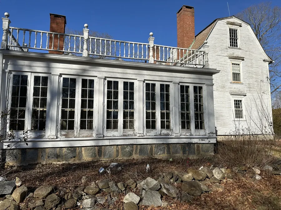 The one-story sunroom addition on the south side, with its rooftop balustrade intact above a wall of windows