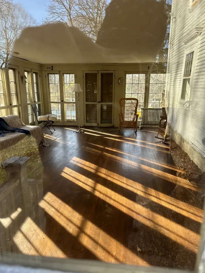 Afternoon light through the sunroom's windows, falling across the hardwood floor and wicker furniture