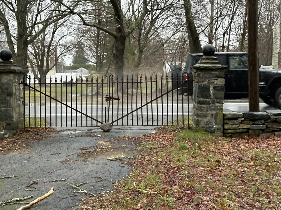 Wrought-iron gates set into the historic stone wall along the road, with cannonball finials on the piers